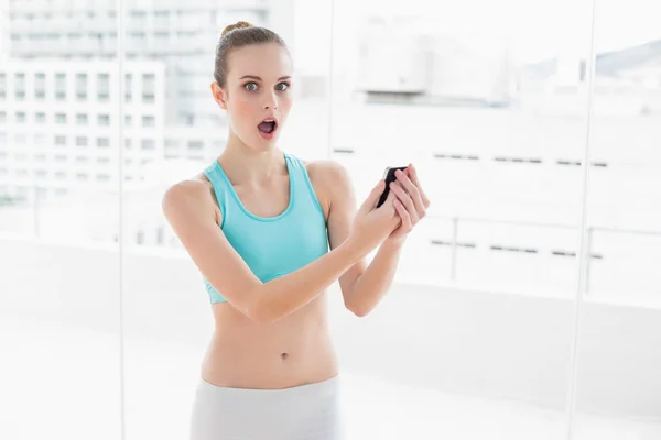 Deportiva mujer sorprendida sosteniendo teléfono inteligente — Foto de Stock