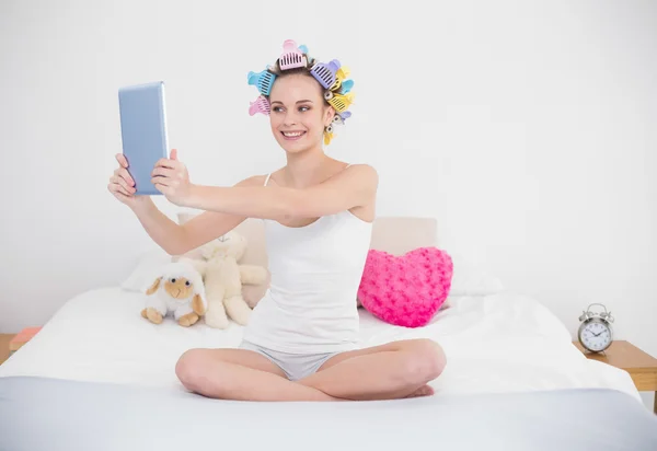 Cheerful woman in hair curlers taking picture of herself with a tablet — Stock Photo, Image