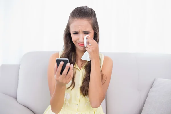 Huilen brunette bedrijf mobiele telefoon en weefsel — Stockfoto