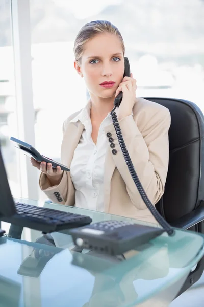 Serious blonde businesswoman on the phone holding calculator — Stock Photo, Image