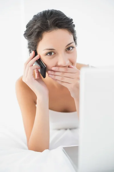 Chockad casual brunett i vit pyjamas att göra ett telefonsamtal — Stockfoto