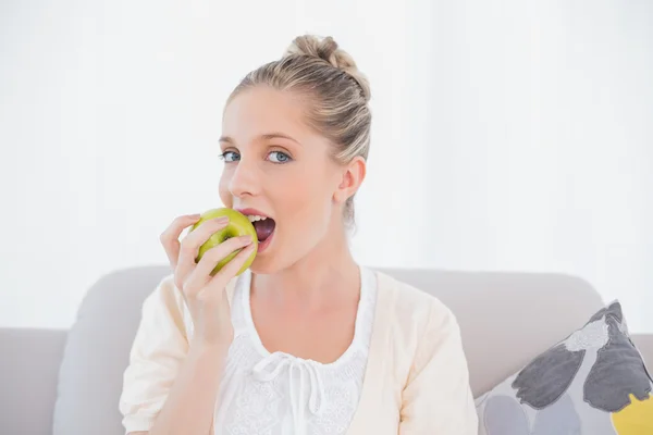 Hermosa modelo comiendo manzana verde sentado en el sofá —  Fotos de Stock