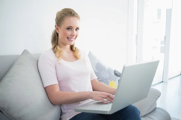 Casual happy blonde sitting on couch using laptop — Stock Photo, Image