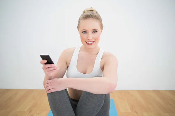 Smiling sporty blonde holding smartphone — Stock Photo, Image