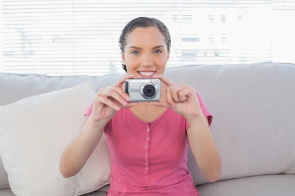 Smiling woman sitting on sofa taking a picture — Stock Photo, Image