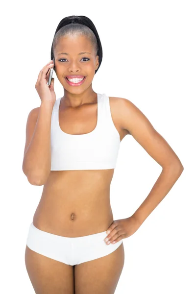 Подтянутая женщина в спортивной одежде разговаривает по телефону, улыбаясь в камеру — стоковое фото