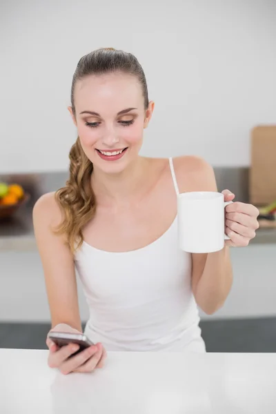 Glad ung kvinna håller en mugg och textilen med smartphone — Stockfoto