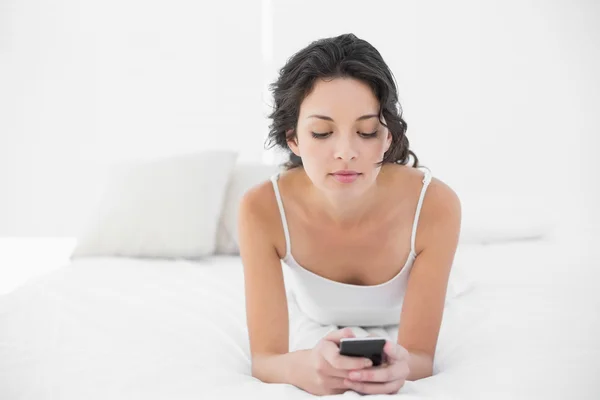 Relajado casual morena en pijama blanco mensajes de texto con un teléfono móvil — Foto de Stock