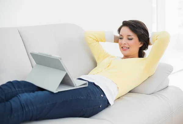 Relaxed casual brunette in yellow cardigan looking at a tablet pc — Stock Photo, Image