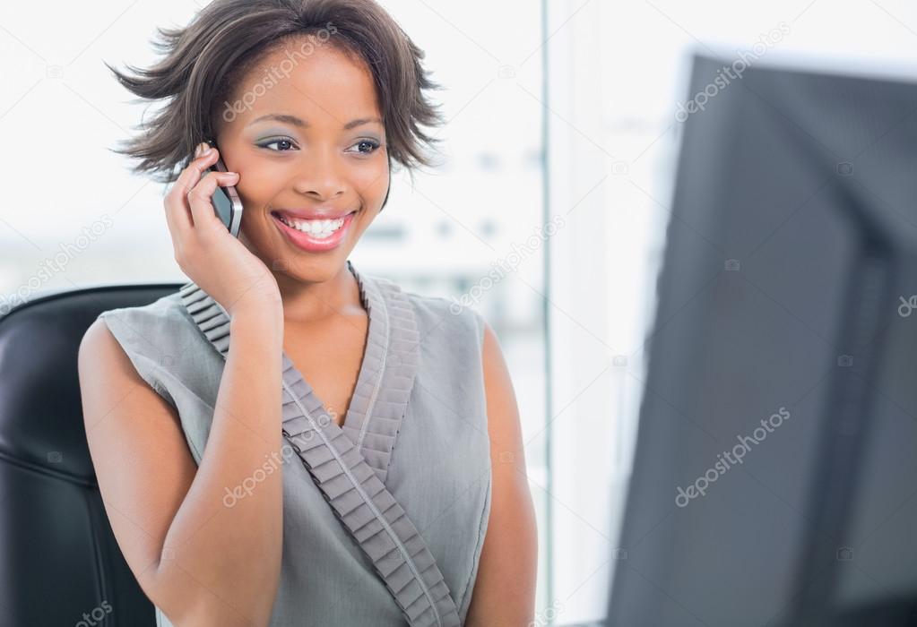 Smiling businesswoman talking on phone while looking at computer screen