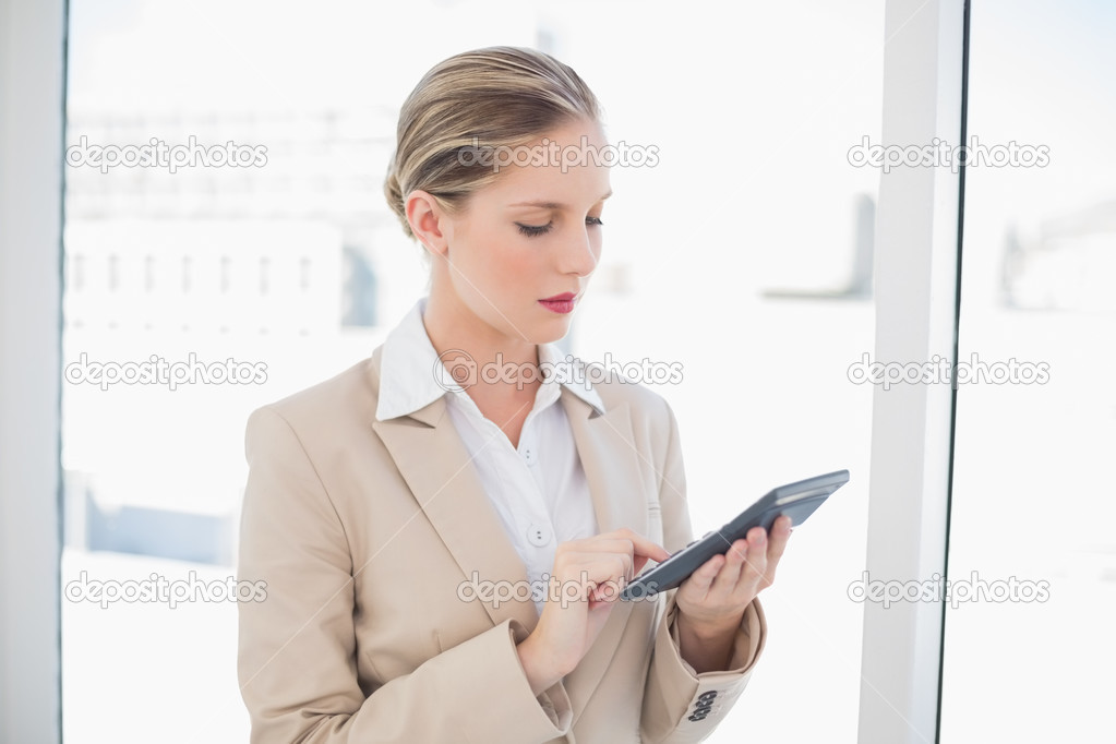 Focused blonde businesswoman using calculator