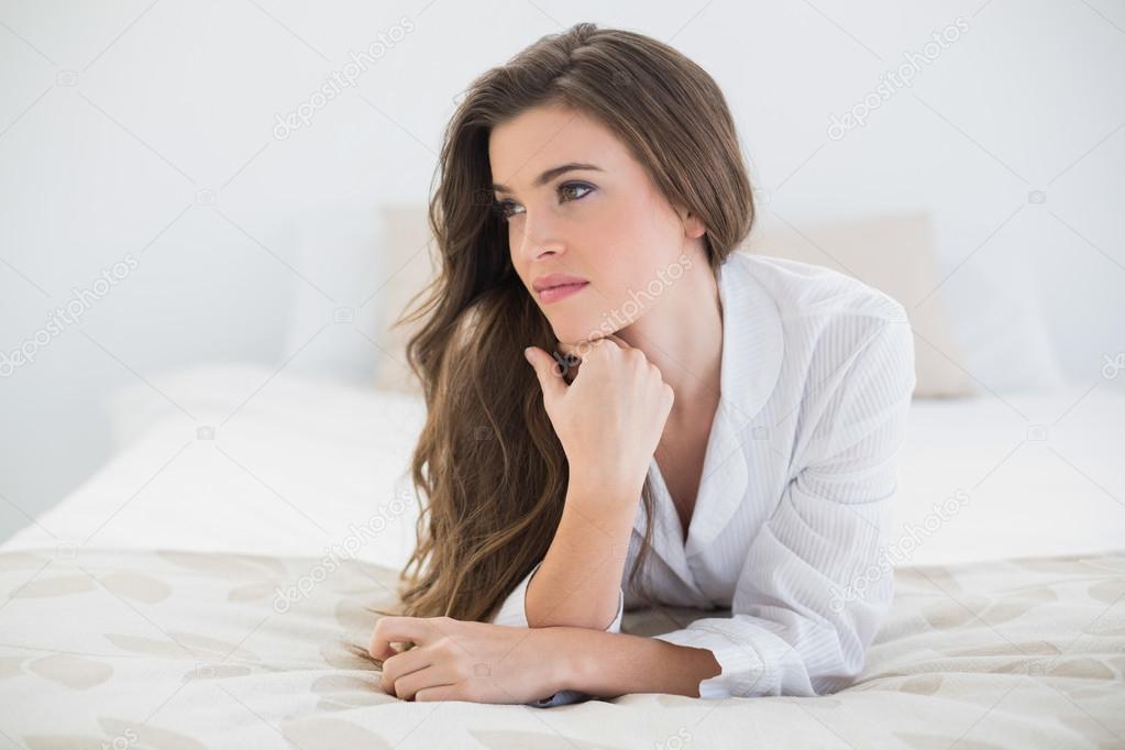 Thinking woman in white pajamas lying on her bed