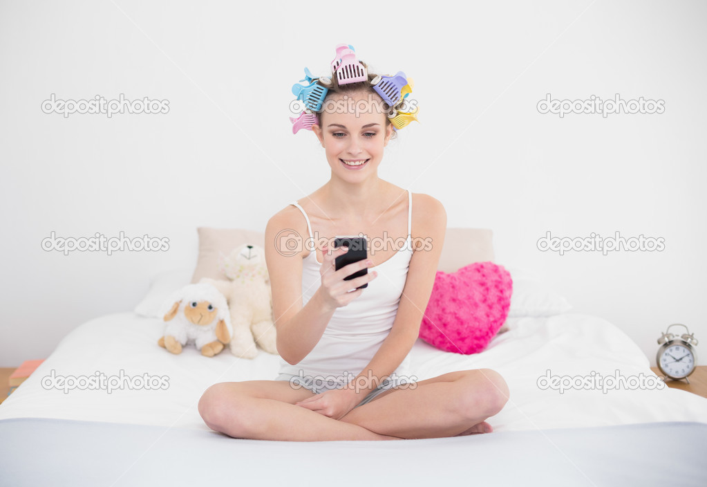 Smiling woman in hair curlers using her mobile phone