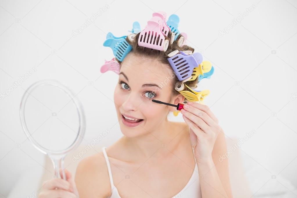 Cheerful woman in hair curlers applying mascara
