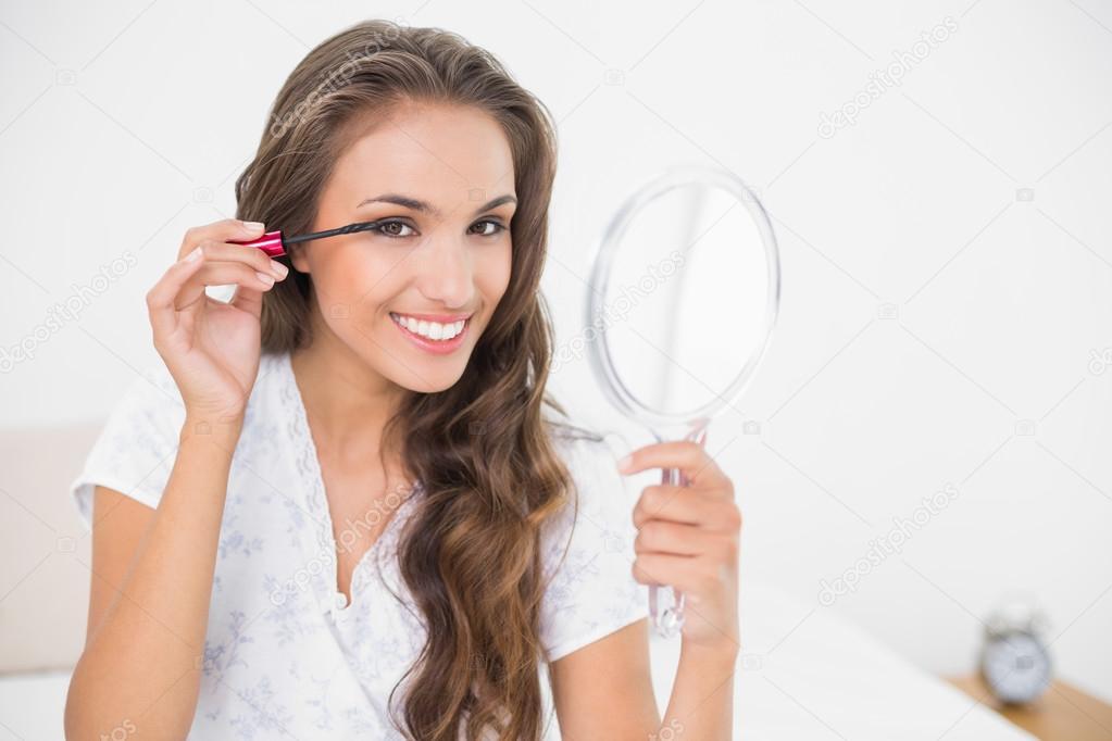 Brunette applying mascara and holding mirror