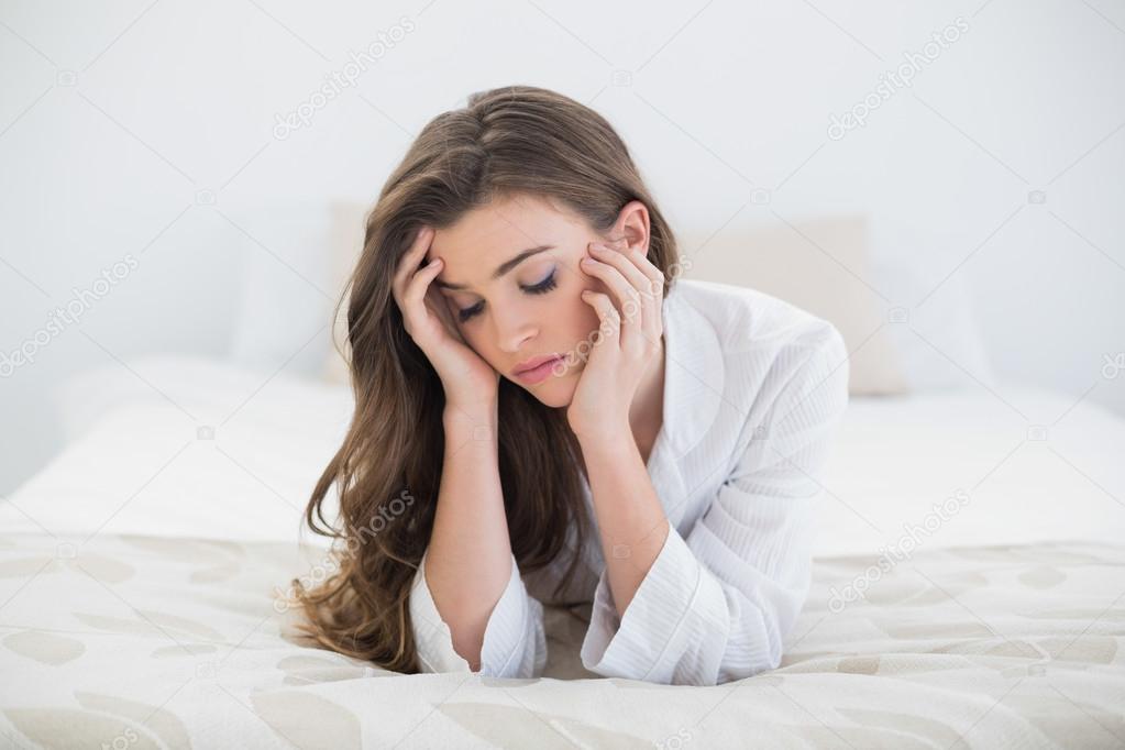 Sad woman in white pajamas lying on her bed