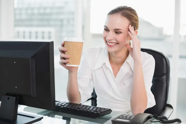 Mujer de negocios sonriente sosteniendo taza desechable sentado en el escritorio — Foto de Stock