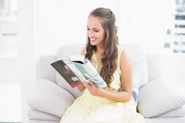 Smiling attractive brunette reading a magazine — Stock Photo, Image