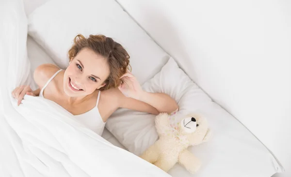 Smiling brunette sitting next to teddy bear — Stock Photo, Image