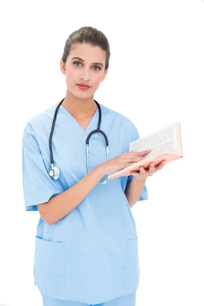 Závažné zdravotní sestra v modrém drhne, držící knihu — Stock fotografie