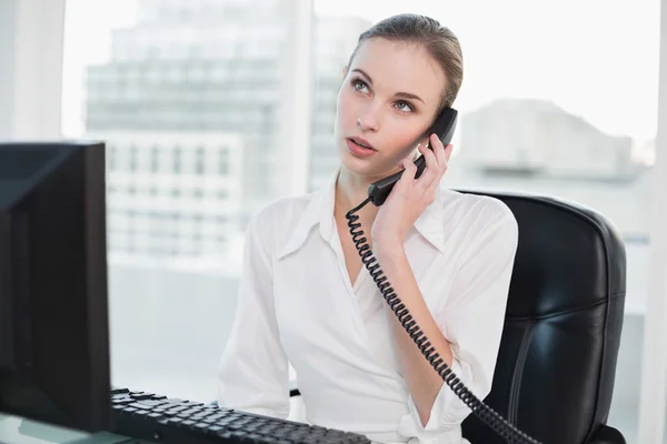 Thoughtful businesswoman sitting at desk on the phone — Stock Photo, Image