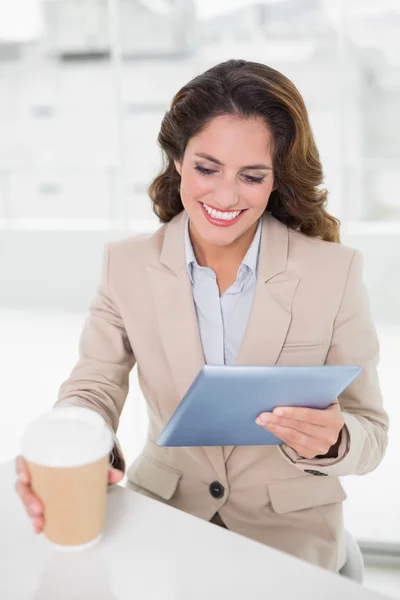 Felice donna d'affari utilizzando tablet digitale alla sua scrivania in possesso di tazza usa e getta — Foto Stock