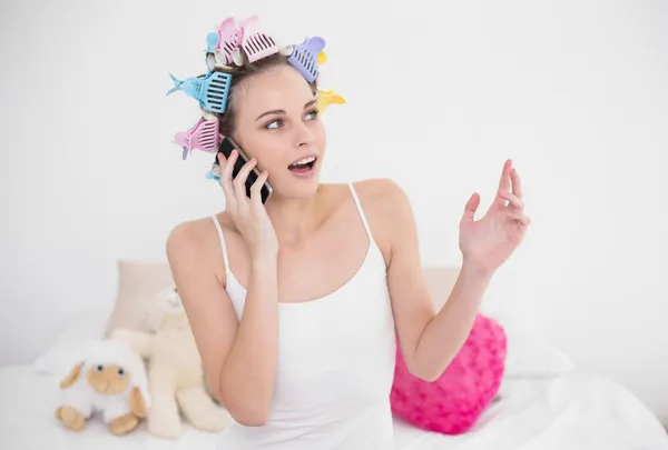 Mulher surpresa em encrespadores de cabelo fazendo um telefonema — Fotografia de Stock