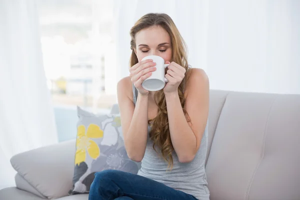 Content young woman sitting on sofa drinking from a mug — Stock Photo, Image