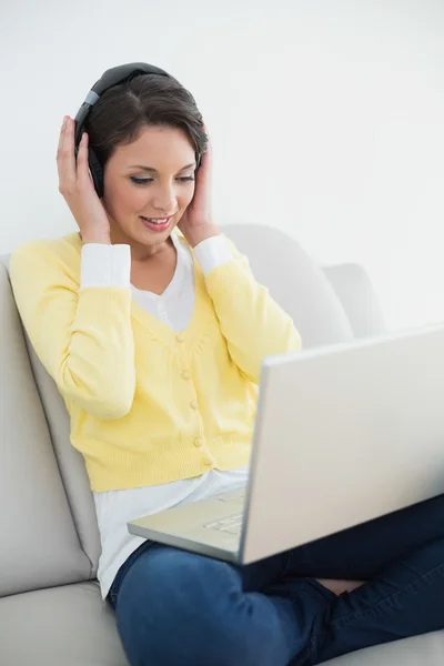 Relajada morena casual en cárdigan amarillo escuchando música mientras usa un portátil —  Fotos de Stock