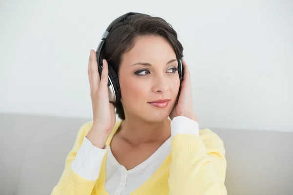 Thoughtful casual brunette in yellow cardigan listening to music with headphones — Stock Photo, Image