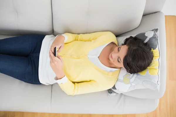 Peaceful casual brunette in yellow cardigan using a mobile phone — Stock Photo, Image