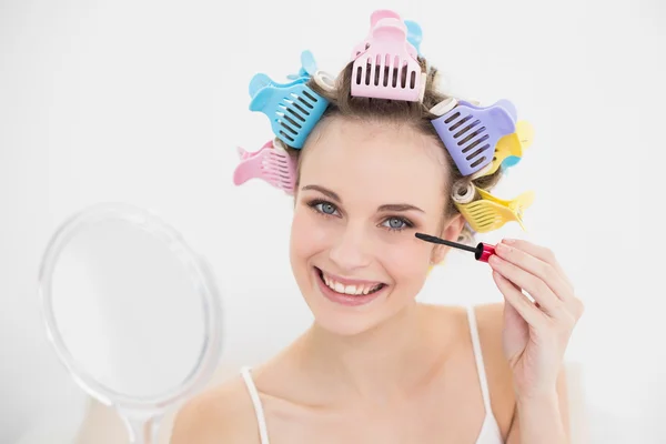 Pretty woman in hair curlers applying mascara — Stock Photo, Image