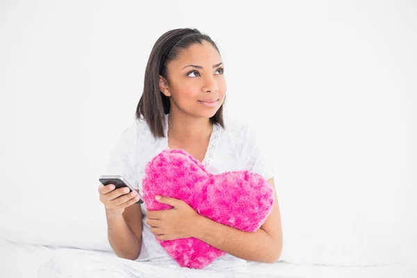 Doordachte jonge model holding een kussen en een mobiele telefoon — Stockfoto