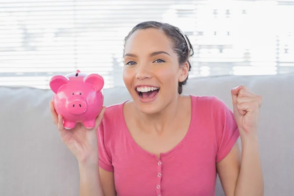 Smiling woman sitting on sofa and holding piggy bank