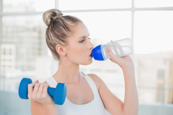 Friedliche sportliche Blondine trinkt Wasser beim Hantelheben — Stockfoto