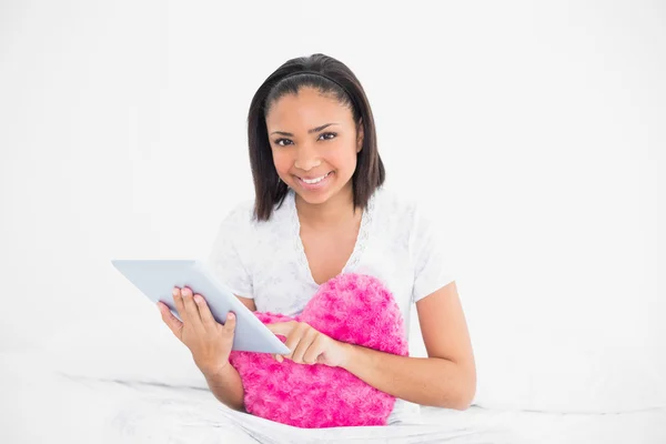 Pleased young model cuddling a pillow and using a tablet pc — Stock Photo, Image