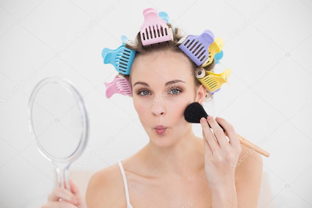Funny woman in hair curlers applying powder on her face