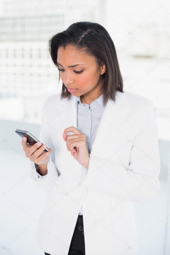 Thinking young businesswoman looking at her mobile phone