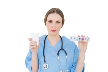 bir plastik kap ve kameraya bakarak tıp tutan genç bir kadın doktor