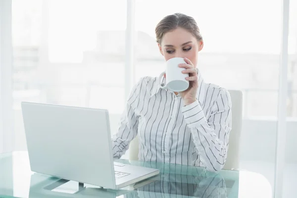 Красивая деловая женщина сидит за своим столом и пьет из чашки — стоковое фото