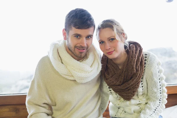 Couple in winter clothing sitting against window — Stock Photo, Image