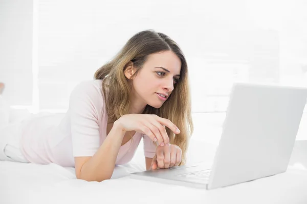 Mooie brunette vrouw met behulp van haar notitieblok liggend op haar bed — Stockfoto