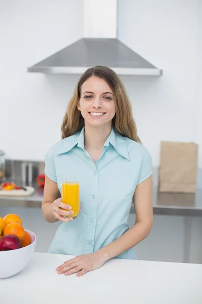 Hermosa mujer morena posando de pie en la cocina sosteniendo un vaso de jugo de naranja — Foto de Stock