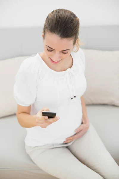 Mulher grávida casual usando seu smartphone tocando sua barriga — Fotografia de Stock