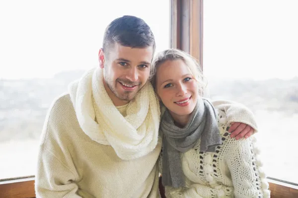 Couple in winter clothing sitting against window — Stock Photo, Image