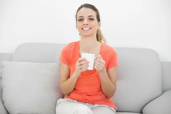 Mulher bonita alegre segurando um copo sentado no sofá — Fotografia de Stock