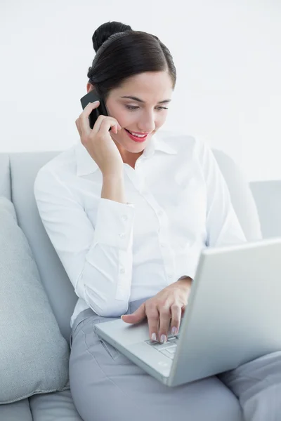 Goed geklede vrouw met laptop en mobiele telefoon op sofa — Stockfoto