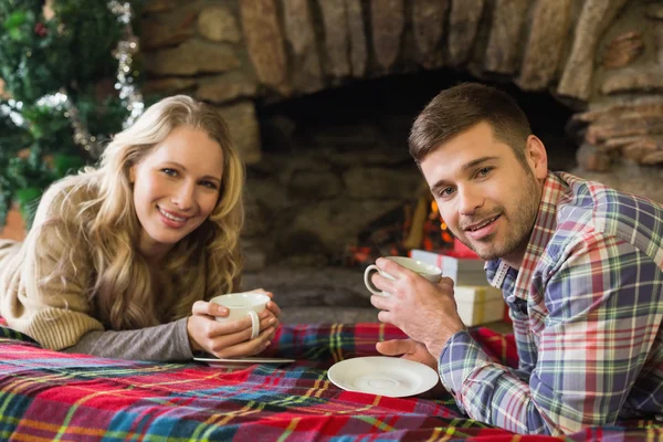 Smiling couple with tea cups in front of lit fireplace — Stock Photo, Image