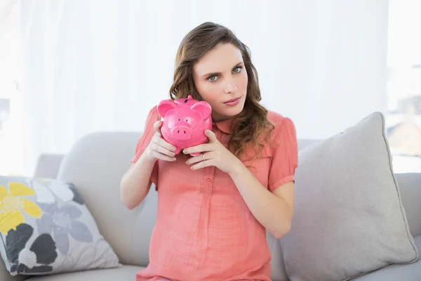 Beautiful pregnant woman shaking a piggy bank sitting on couch — Stock Photo, Image