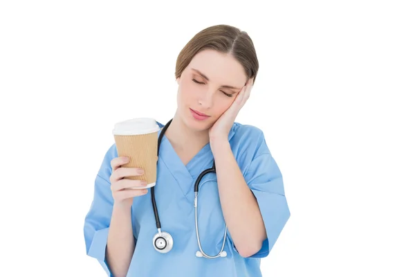 Female doctor holding a coffee mug and lifting her hand to her face — Stock Photo, Image